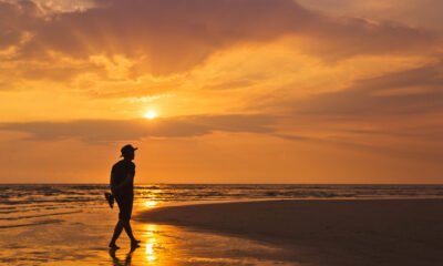 orange sky with silhouette of man in a hat walking on the beach